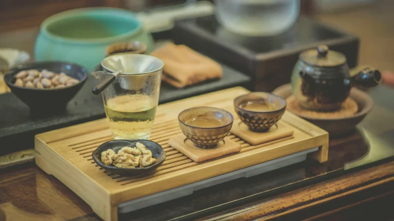 Plateau de dégustation de thé avec une théière en céramique, deux tasses de thé, une tasse en verre contenant du thé vert, et des noix servies dans une petite coupelle, sur une table en bois dans un cadre chaleureux et raffiné.
