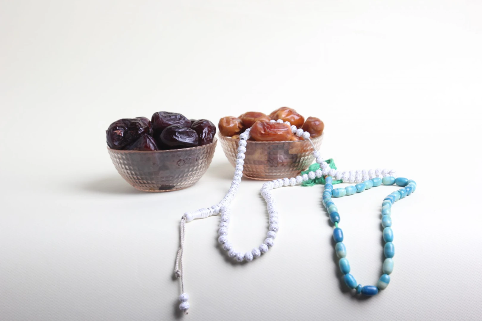 Deux bols de dattes Ajwa et sukari avec chapelets de prière sur fond clair