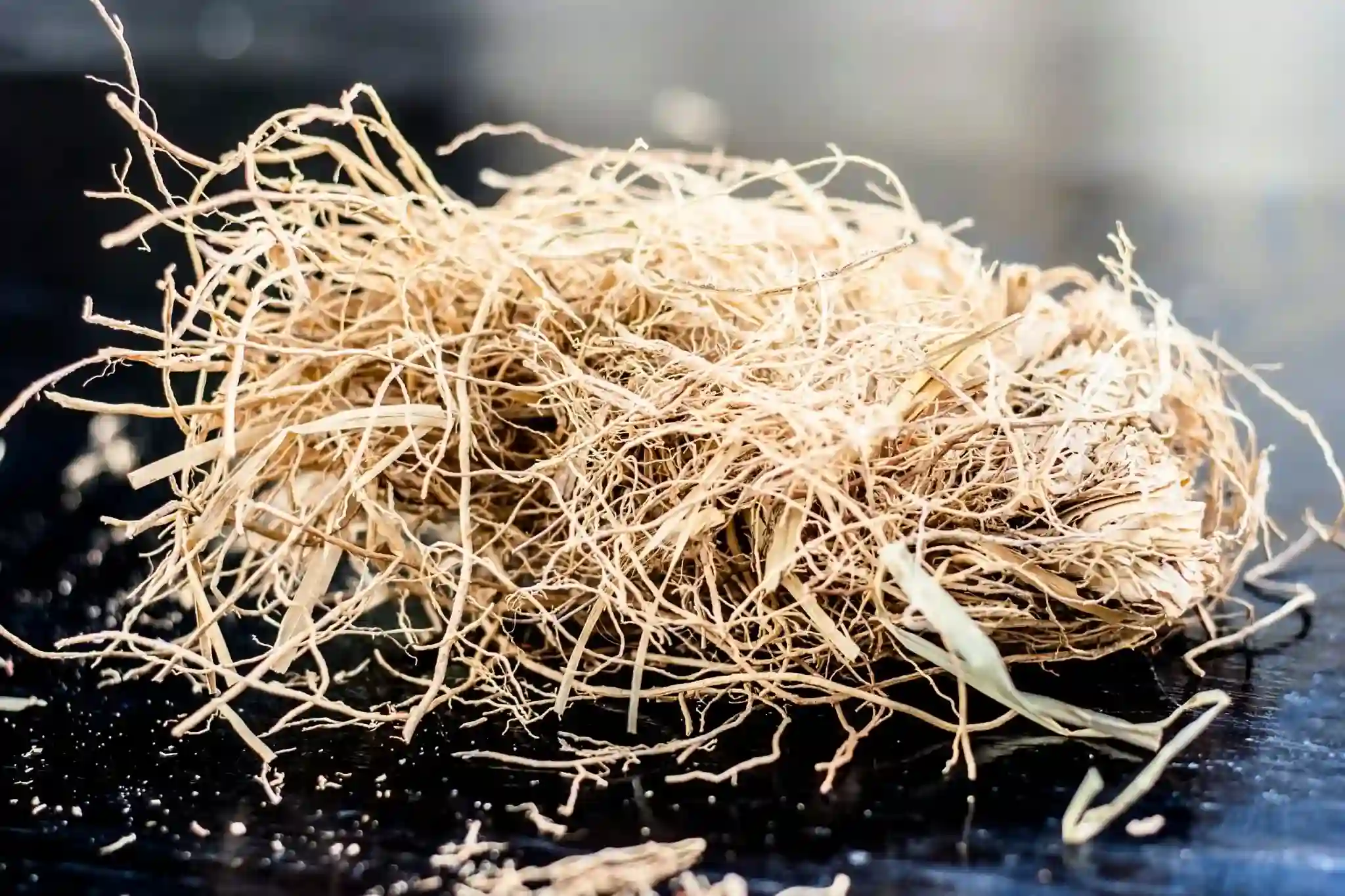 Tas de racines de vétiver brutes et sèches posées sur une surface sombre, prêtes à être utilisées pour infusions ou huiles essentielles.