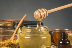 Miel brut doré dans un pot en verre avec cuillère doseuse, carnet et balance de cuisine pour illustrer l’équilibre entre plaisir sucré et contrôle du poids.