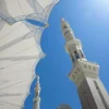 Minarets blancs de la Mosquée du Prophète (Masjid Al-Nabawi) s'élançant vers un ciel bleu intense, avec les voiles tendues du parvis au premier plan, Médine, Arabie Saoudite