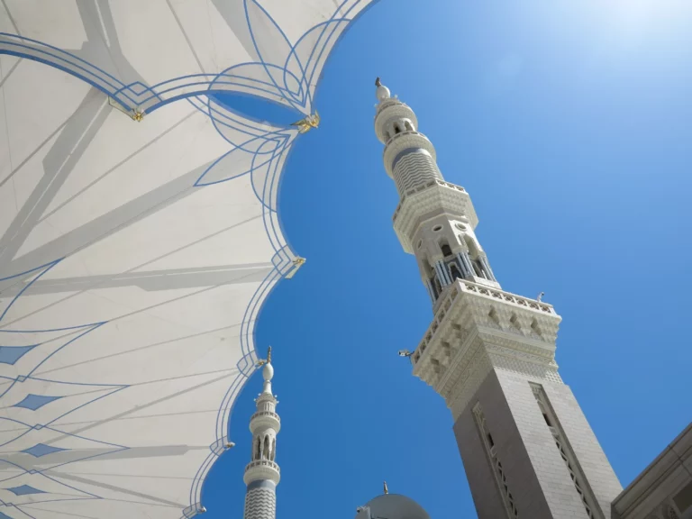 Minarets blancs de la Mosquée du Prophète (Masjid Al-Nabawi) s'élançant vers un ciel bleu intense, avec les voiles tendues du parvis au premier plan, Médine, Arabie Saoudite